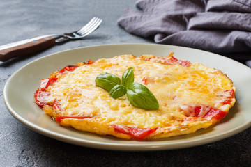 Omelet, scrambled eggs with tomatoes and cheese in a plate on a dark table.