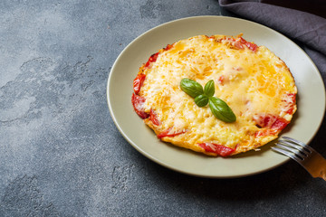 Omelet, scrambled eggs with tomatoes and cheese in a plate on a dark table.