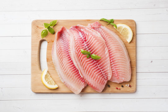 Raw fish fillet of tilapia on a cutting Board with lemon and spices. White  table with copy space. Stock Photo