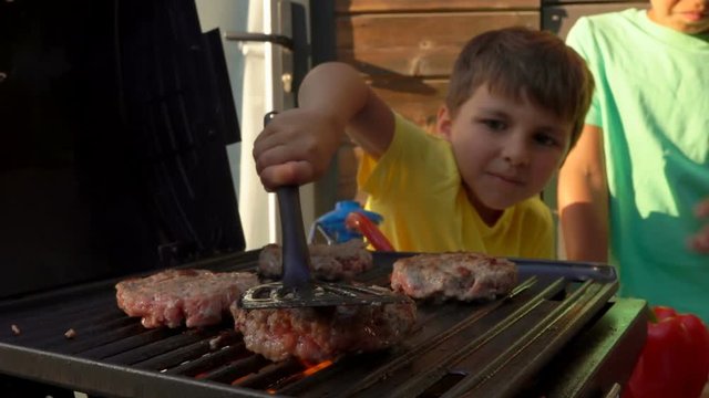 Boy presses the cutlet on the grill with a spatula.