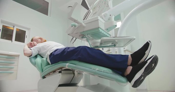 Portrait Of Male Dentist Sleeping At Work On Dental Chair During Break.