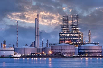 Fototapeten Petrochemical industry next to a river with a dramatic cloudy sky at twilight, Port of Antwerp, Belgium. © tonyv3112