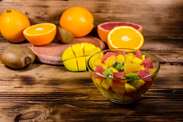 Salad with mango, oranges, grapefruit and kiwi fruits in a glass bowl on wooden table