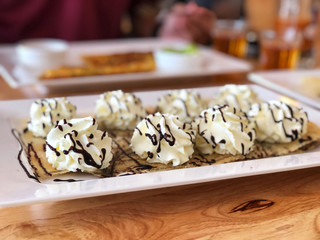slim crispy roti  topped with whipped cream and chocolate sauce  in white plate on the wooden table.