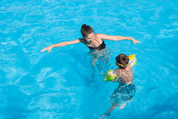 beautiful young adult happy mother woman teaching her little kid to swim in summer azure pool during holiday travel