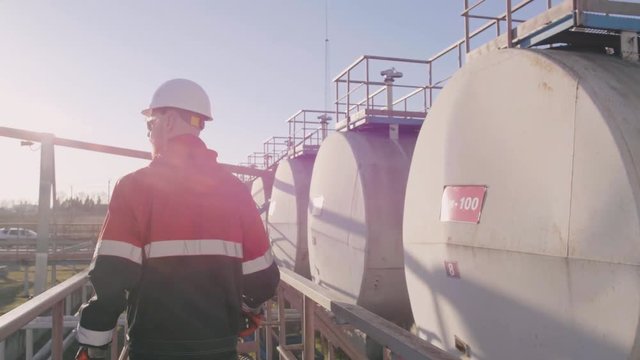 Petrochemical engineer walks along row of cisterns with oil and controls their condition.