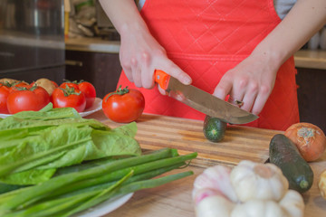 Chef cuts the vegetables into a meal. A woman uses a knife and cooks. Woman's hands cutting vegetables, behind fresh vegetables