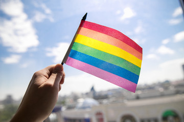 Gay man holding rainbow LGBT flag against blue sky.