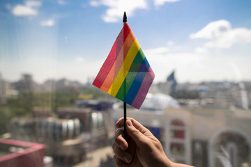 Gay man holding rainbow LGBT flag against blue sky.
