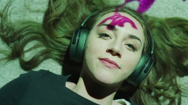 Close up of woman laying on floor listening to headphones illuminated by purple flowing color / Cedar Hills, Utah, United States