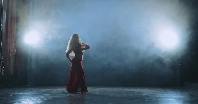 Beautiful blonde girl dancing arabic dance in tubers of smoke. Silhouette of oriental dance.