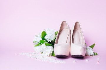 Wedding shoes and bouquet lying on pink background. Close up