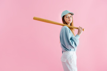 pretty teenage girl in cap holding wooden baseball bat isolated on pink