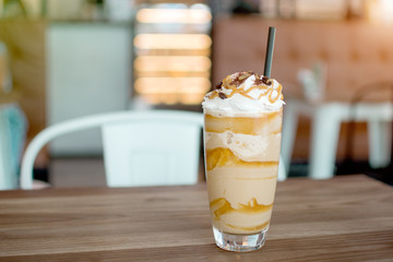 Iced frappe with whipped cream and caramel syrup, with straws and grains of coffee in a tall glass...