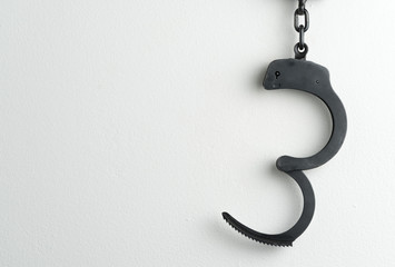 Unlocked police handcuffs on a white painted wall. Potential copy space to the left of handcuffs.