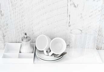 Coffee and tea making set of white cups, saucers, tea spoons and glasses on white porcelain tray. Hotel accomodation. Copy space.
