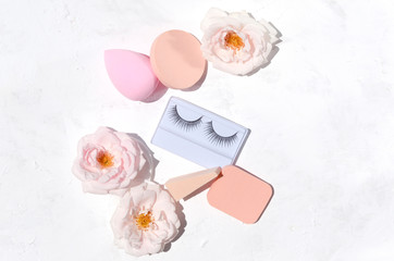 Beautiful pink roses, cosmetic sponge and false eyelashes on the white background.Concept of beauty tools for women