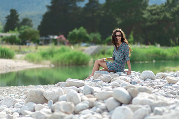 Woman is sitting near the river or lake. 