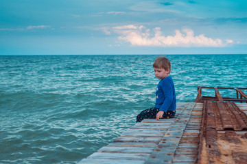 Fototapeta na wymiar A little boy is sitting on the pier at sea.