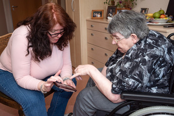 Seniorin im Rollstuhl mit Frau im Dialog im Heimzimmer