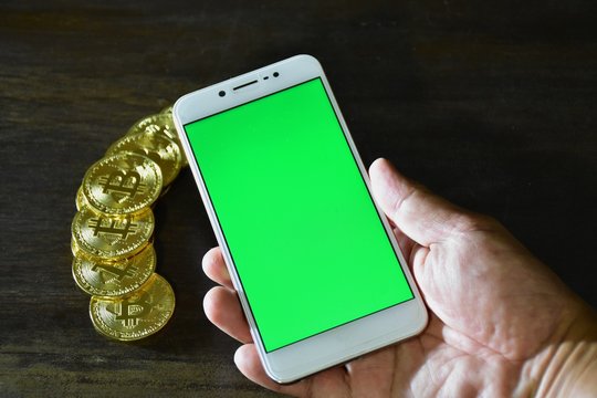 Smart phone a green screen in the background, there are many coins of bits Coyne.