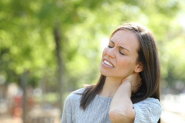 Woman suffering neck ache outdoors in a park