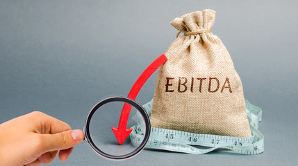 Money bag with the word Ebitda and down arrow. Earnings before interest, taxes, depreciation and...