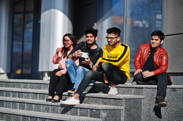 Fototapeta premium Group of asian people friends sitting on stairs outdoor against modern building and making selfie by phone.