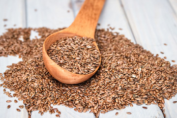 Flax seeds in a wood spoon on a wooden background.Linseed is scattered.