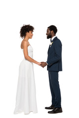 happy african american bridegroom and bride holding hands while looking at each other isolated on white