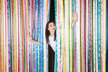 Cheerful young woman stretching out her hands at celebration party on colourful rainbow fribbons background Birthday or New Year eve celebrating concept.