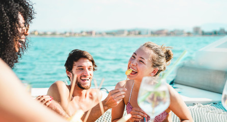 Fototapeta premium Happy rich friends drinking tropical cocktail and eating pineapple in boat party - Young people having fun in sail tour - Youth lifestyle, travel and summer concept - Focus on blond girl face