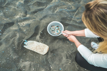 Young woman cleaning microplastics from sand on the beach - Environmental problem, pollution and...