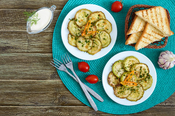Tasty fried zucchini slices on a plate with sauce on a wooden table. Picnic snack. Rustic style. Top view, flat lay.