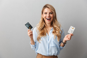 Pretty blonde business woman posing isolated grey wall background holding two credit cards.