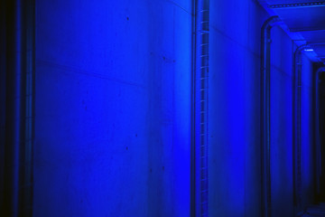Perspective view of ventilation pipes and concrete wall at parking garage lit with blue light