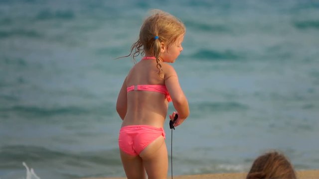 Cheerful girl drags a toy on the sand.