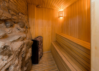 Inside of a modern day sauna, rock wall and wooden benches to si