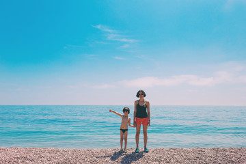 A boy with his mother standing on the beach and looking at the sea.