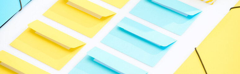panoramic shot of yellow and blue folders and opened envelopes on white background