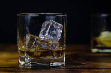 Whiskey / cognac glass with ice on a wooden background. Dark backdrop