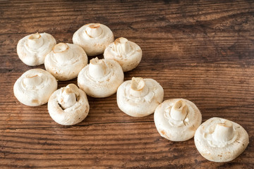 A row of large whit  mushrooms placed across a dark oak planked board