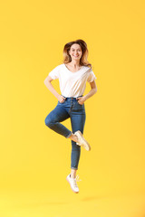 Jumping young woman in jeans on color background