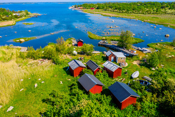 Small red fishing sheds among shrubs at the end of a shallow bay. Location on the island Hasslo in Blekinge archipelago, Sweden. - 272614434