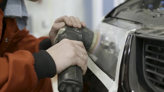 Close up for auto mechanic buffing and polishing car head. light. Art. Worker polishing the headlight of a car at automobile repair and renew service station, using a professional power buffer machine