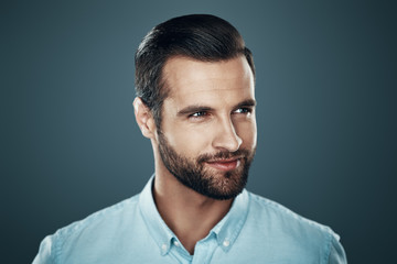 Fototapeta premium Male beauty. Handsome young man smiling and looking away while standing against grey background
