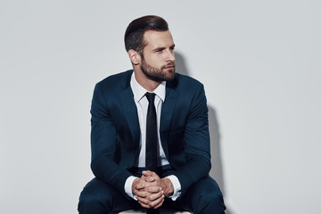 Time to make decision. Handsome young man looking away while sitting against grey background