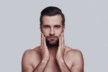 Need to shave. Handsome young man keeping head in hands while standing against grey background
