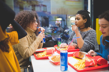 group of young multiracial women eating in fast food and having conversation