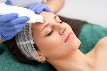 Obraz na płótnie Canvas Beautiful young woman having ultrasound cleansing treatment facial procedure by professional cosmetologist at beauty salon spa center skincare youth pampering smooth ultrasonic